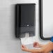 A woman using a black Tork wall-mount multifold hand towel dispenser.