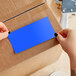A person's hands cutting a light blue rectangular piece of paper from a box.