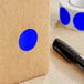 A roll of Lavex dark blue paper inventory labels with blue circles on a brown surface next to a black pen.