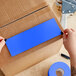 A person's hands cutting a light blue rectangular piece of paper.