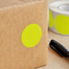 A roll of Lavex 1 1/2" round chartreuse inventory labels with yellow dots on a brown surface next to a pen.