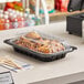 A tray of chicken in a Pactiv black chicken barn on a counter.