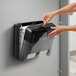 A person's hands putting a roll of Tork toilet paper into a black and silver Tork dispenser