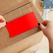 A person using two hands to apply a red rectangular Lavex inventory label to a cardboard box.