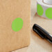 A roll of Lavex fluorescent green round inventory labels with white and green stickers on a brown surface next to a black pen.