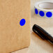 A roll of Lavex dark blue round inventory labels with a semi-gloss finish with a blue dot on a brown surface next to a black pen.
