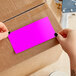 Two hands holding a rectangular pink paper label.