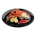 A Tablecraft Sierra Collection black melamine serving platter with crab legs and lemon slices on it.