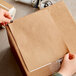 A person with black nails using a piece of Lavex Natural Kraft Paper to label a cardboard box.