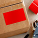 A cardboard box with a red label reading "Lavex 3" x 5" Standard Red Semi-Gloss Paper Permanent Rectangular Inventory Label"