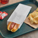 A hot dog in a Bagcraft white paper bag on a tray with chips.