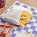 A bag of Bagcraft white french fries on a checkered table with ketchup packets.