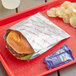 A hamburger in a Bagcraft foil wrapper on a red tray.