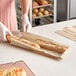 A person in gloves is cutting a baguette in a Bagcraft Natural Artisan Print bread bag.