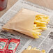 A Bagcraft EcoCraft natural paper bag filled with french fries on a newspaper.