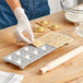 A person using an Imperia RavioChef ravioli mold to make ravioli and put it into a pan.