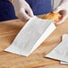 A person in gloves putting a sandwich in a white Bagcraft paper bag.