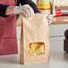 A person in gloves holding a Bagcraft paper bag with tortilla chips and a window.