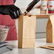 A person in black gloves pouring coffee beans into a brown Bagcraft coffee bag.