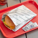 A Bagcraft paper bag with a cheeseburger and condiments on a red tray.