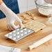 A person using the Imperia RavioChef ravioli mold to make ravioli on a wooden table.