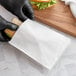 A person in black gloves putting a sandwich in a white Bagcraft sandwich bag.