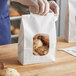 A person holding a Bagcraft white stand-up bakery bag with cookies inside.