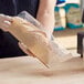 A hand holding a Bagcraft clear deli bag of bread over a wooden bakery display counter.