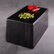A rectangular black and faux zebra wood display riser with red peppers on it.