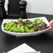 A person holding an American Metalcraft oval stoneware bowl of salad.