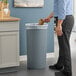 A man standing next to a Lavex Gray round wastebasket in a corporate cafeteria.