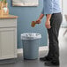 A man in a professional kitchen pouring coffee into a Lavex gray round wastebasket.