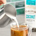 A person pouring Califia Farms Barista Blend Coconut Milk into a glass of coffee.