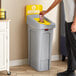 A person putting a bottle into a white Rubbermaid Slim Jim single-stream recycling station.