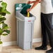 A woman putting a plastic bag in a white Rubbermaid Slim Jim trash can.