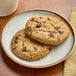 Two Red Plate Foods vegan chocolate chip cookies on a white plate.