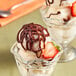 A glass bowl of ice cream with strawberries and chocolate drizzled on top.