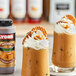 A glass of iced coffee with whipped cream and Lyons Sweet Indulgence Bourbon Caramel sauce on a table.