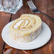 A slice of rolled sponge cake with cream filling on a round cream-colored porcelain plate.