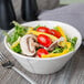 A Libbey round cream porcelain serving bowl filled with salad with tomatoes and peppers and a fork.