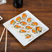 A Libbey white porcelain plate with sushi and chopsticks on it.