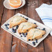 A rectangular cream porcelain tray displaying three blueberry scones, surrounded by fresh blueberries.