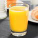 A Libbey juice glass filled with orange juice on a table in a diner.