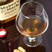 A Libbey brandy glass filled with liquid next to a bottle of peanuts.