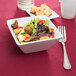 A Libbey Ultra Bright White Square Porcelain Bowl filled with salad with a fork and knife on a table.