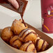 A person pouring Clown chocolate icing onto a doughnut.