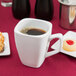 A Libbey tall white porcelain cup of coffee and a pastry on a table.