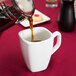 A person pouring coffee into a Libbey Ultra Bright White tall porcelain cup.