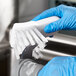 A person in blue gloves cleaning a Vollrath food processor blade with a brush.