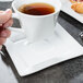 A person holding a cup of tea with a Libbey white porcelain saucer.